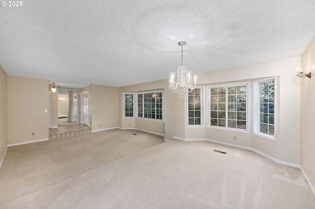 carpeted empty room with visible vents, a notable chandelier, a textured ceiling, and baseboards