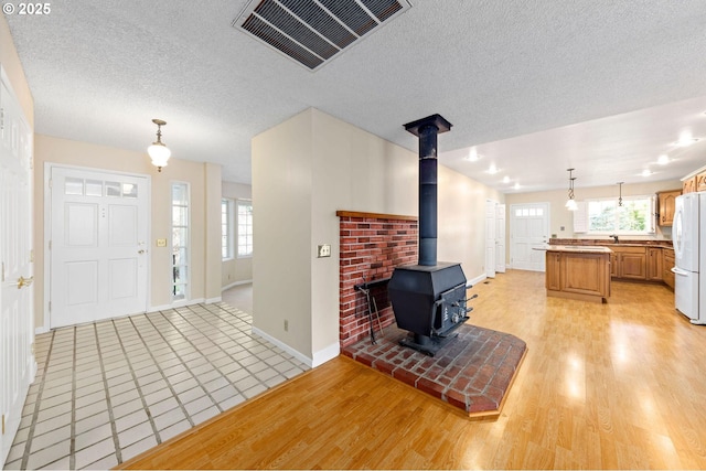 entrance foyer featuring a textured ceiling, a wood stove, light wood-style flooring, and visible vents