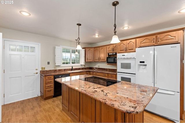 kitchen featuring light wood finished floors, light stone counters, a center island, black appliances, and a sink