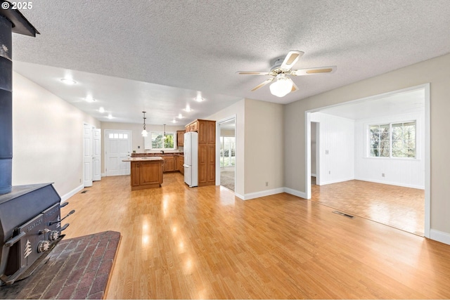 living area with light wood finished floors, baseboards, a ceiling fan, a wood stove, and a textured ceiling