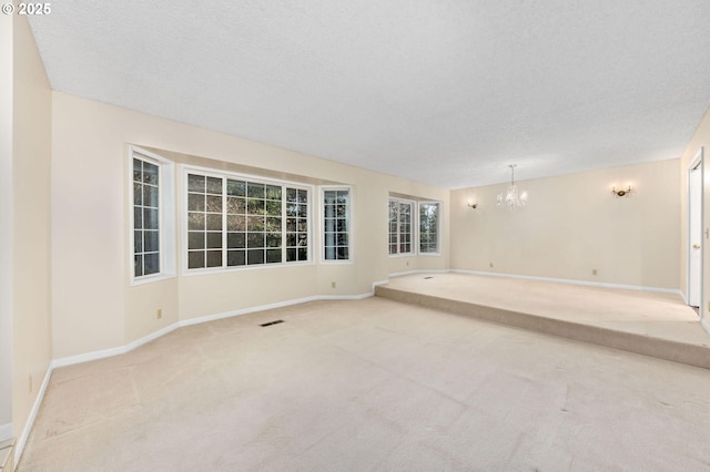 carpeted spare room featuring a chandelier, a textured ceiling, visible vents, and baseboards