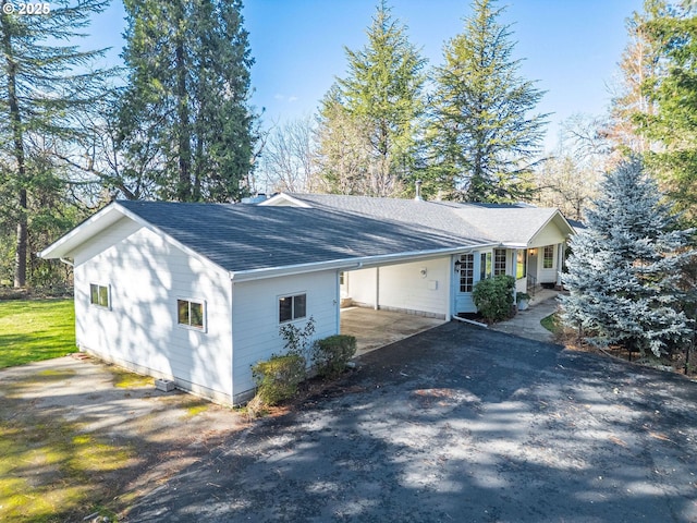 exterior space featuring driveway, a carport, and a shingled roof