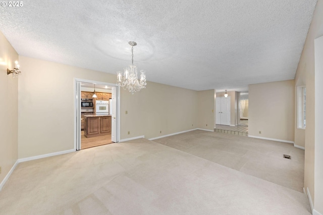 unfurnished room featuring light colored carpet, a textured ceiling, baseboards, and an inviting chandelier