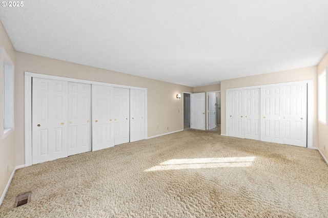 unfurnished bedroom with multiple closets, baseboards, visible vents, and carpet flooring