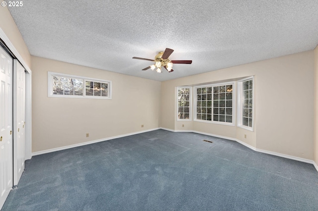 spare room with ceiling fan, a textured ceiling, dark carpet, and baseboards