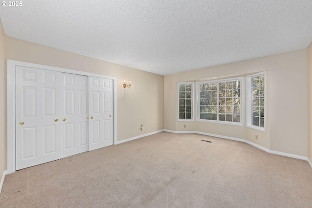 unfurnished bedroom featuring a textured ceiling, carpet, visible vents, and baseboards