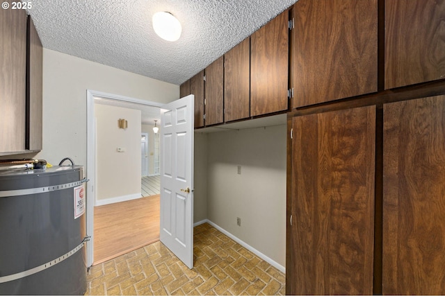 interior space featuring a textured ceiling, brick floor, secured water heater, and baseboards