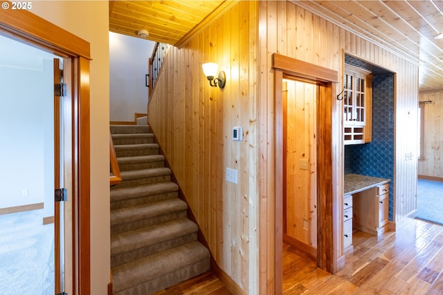 stairs featuring wooden ceiling, wooden walls, baseboards, and wood finished floors