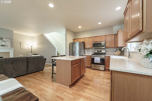 kitchen featuring a kitchen island, appliances with stainless steel finishes, sink, a tiled fireplace, and light hardwood / wood-style floors