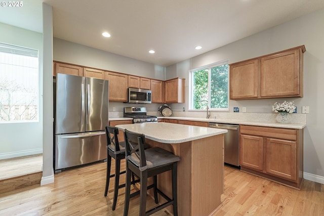 kitchen featuring sink, light wood-type flooring, appliances with stainless steel finishes, a kitchen breakfast bar, and a kitchen island