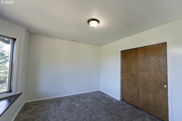 unfurnished bedroom featuring dark carpet, visible vents, and multiple windows