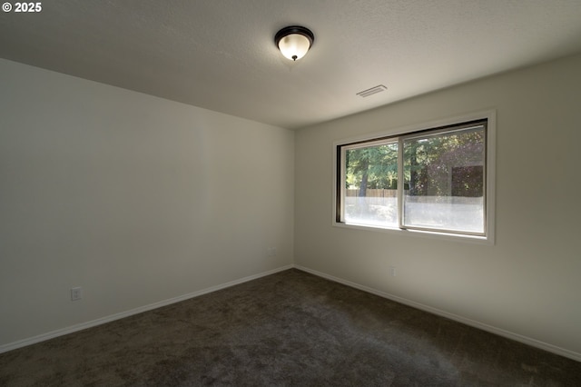 spare room featuring baseboards, dark carpet, and visible vents