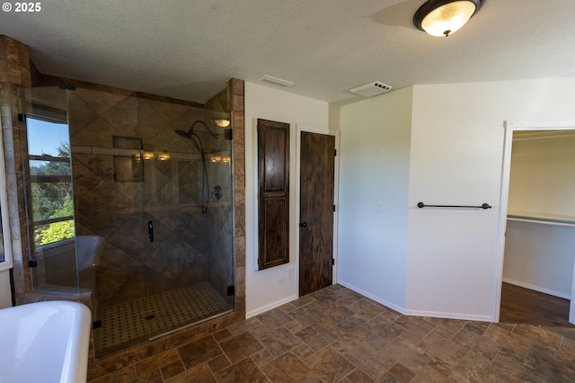 bathroom with visible vents, baseboards, a textured ceiling, a freestanding bath, and a stall shower