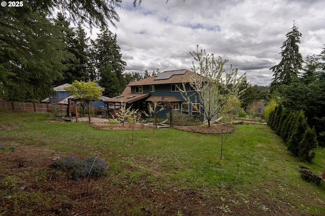 rear view of property featuring roof mounted solar panels, fence, a yard, and a patio area