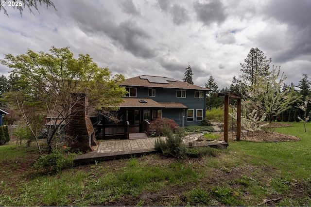rear view of property featuring roof with shingles, a lawn, a deck, a sunroom, and roof mounted solar panels