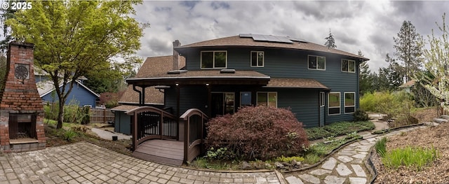 rear view of property featuring a chimney, a patio area, fence, roof mounted solar panels, and an outdoor brick fireplace