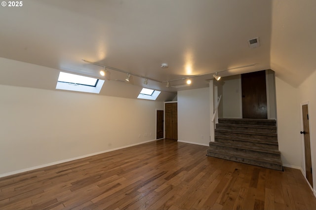 below grade area with track lighting, wood-type flooring, visible vents, baseboards, and stairway