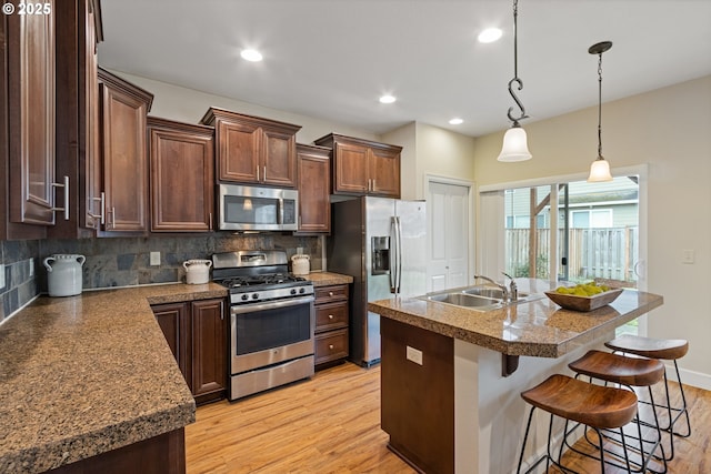 kitchen featuring appliances with stainless steel finishes, backsplash, a breakfast bar, sink, and a center island with sink