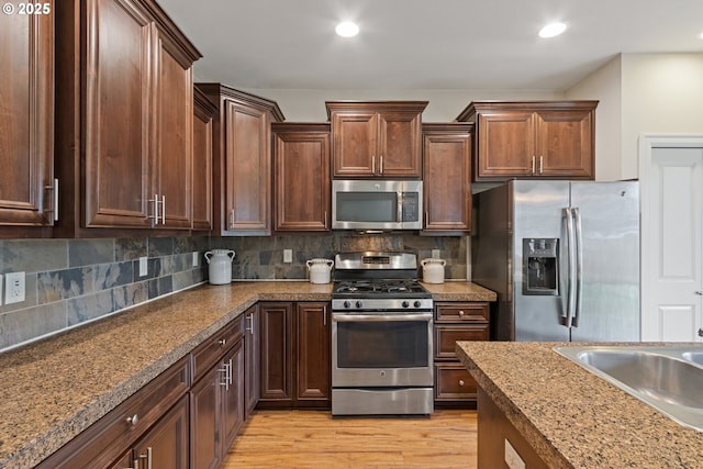 kitchen featuring tasteful backsplash, light stone countertops, stainless steel appliances, and light hardwood / wood-style floors