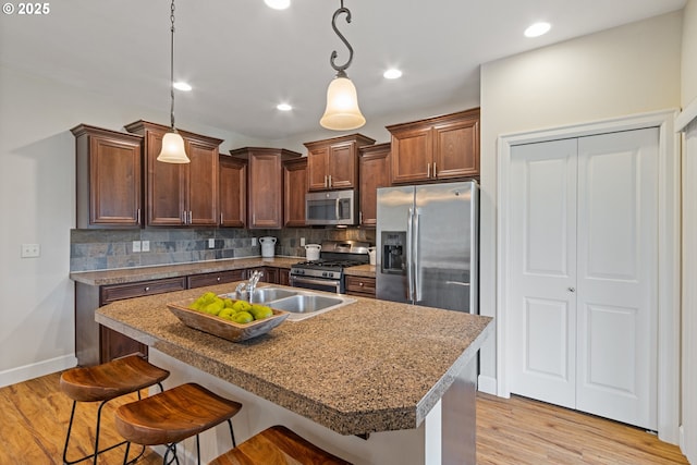 kitchen featuring an island with sink, appliances with stainless steel finishes, tasteful backsplash, decorative light fixtures, and a kitchen bar