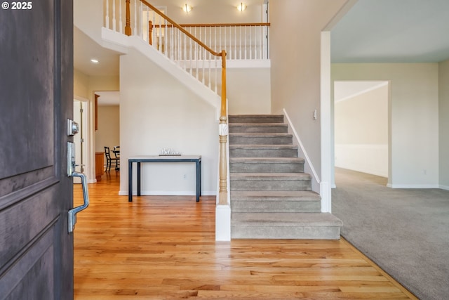 staircase featuring a high ceiling, carpet flooring, wood finished floors, and baseboards