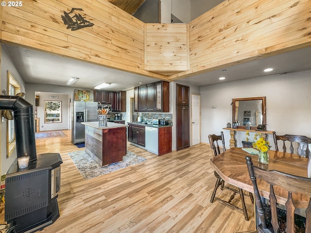 kitchen with stainless steel appliances, a towering ceiling, light countertops, light wood-style floors, and a wood stove