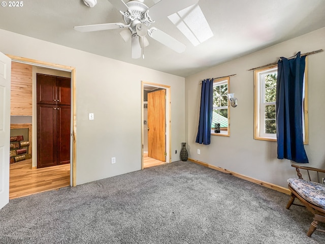 unfurnished bedroom featuring light colored carpet, a skylight, a ceiling fan, and baseboards