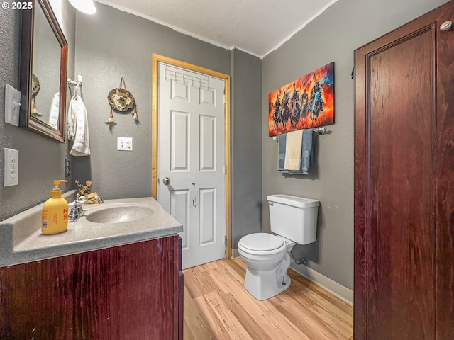 half bathroom featuring wood finished floors, toilet, vanity, and ornamental molding