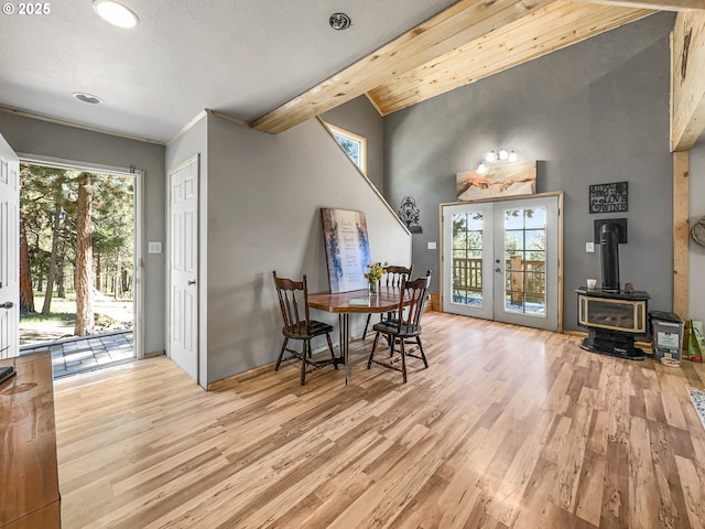 dining area featuring french doors, a wood stove, light wood-type flooring, plenty of natural light, and beamed ceiling