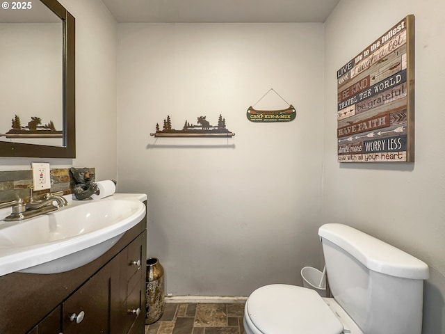 half bath with stone finish flooring, toilet, vanity, and baseboards