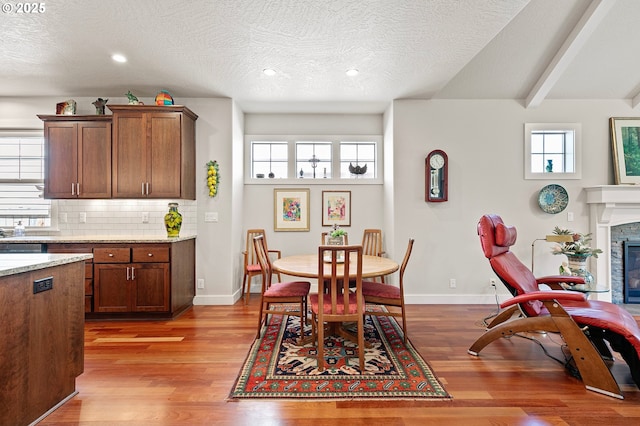 dining room featuring a glass covered fireplace, baseboards, plenty of natural light, and wood finished floors