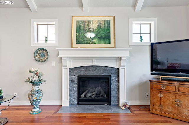 living room featuring wood finished floors, a fireplace with flush hearth, baseboards, and beam ceiling