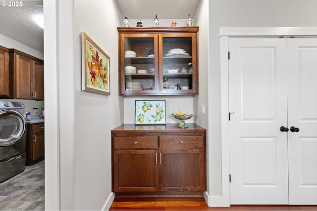 washroom featuring washer / dryer, wood finished floors, baseboards, a textured ceiling, and cabinet space