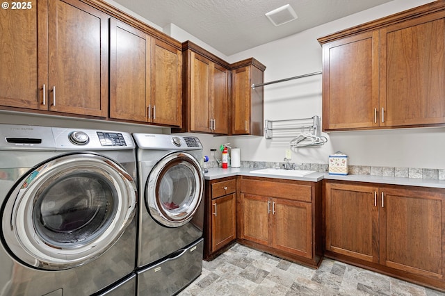 clothes washing area with cabinet space, stone finish flooring, washer and clothes dryer, and a sink