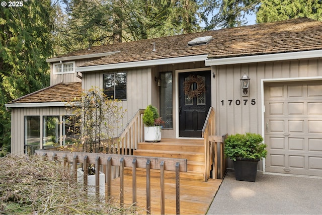 view of exterior entry with a garage, roof with shingles, and board and batten siding