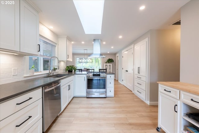 kitchen with stainless steel appliances, a sink, island range hood, light wood-style flooring, and a peninsula