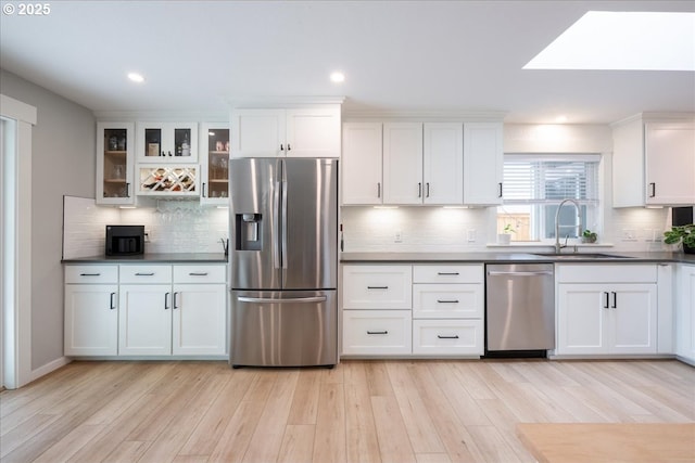 kitchen featuring stainless steel appliances, a sink, dark countertops, white cabinets, and light wood-type flooring
