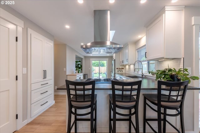 kitchen featuring island range hood, light wood-type flooring, a sink, white cabinets, and recessed lighting