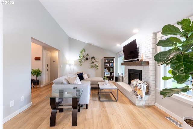 living area with lofted ceiling, light wood finished floors, a fireplace, and baseboards