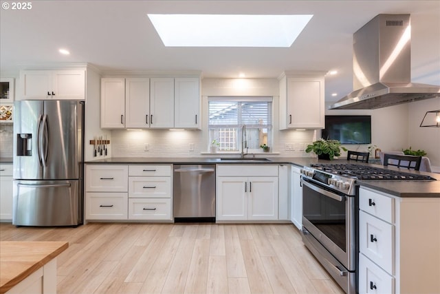 kitchen with appliances with stainless steel finishes, a sink, island exhaust hood, dark countertops, and a skylight
