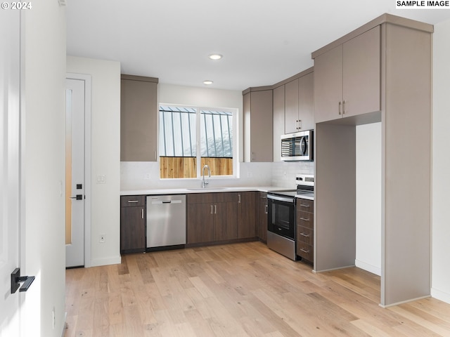 kitchen with sink, light wood-type flooring, tasteful backsplash, and appliances with stainless steel finishes