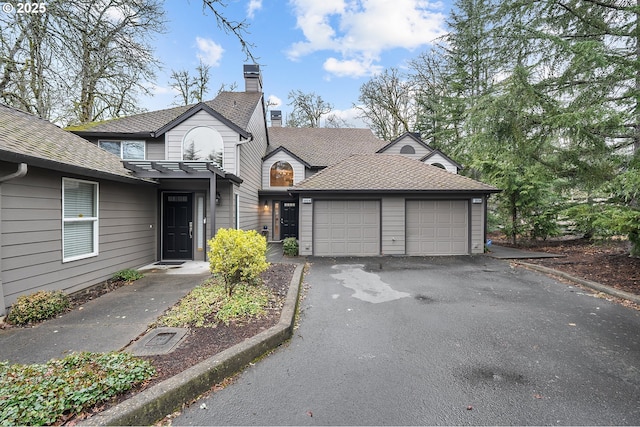 view of front of property with a shingled roof, a garage, driveway, and a chimney