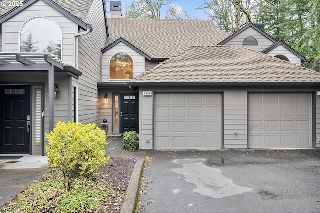 view of front facade featuring aphalt driveway, an attached garage, a shingled roof, and a chimney