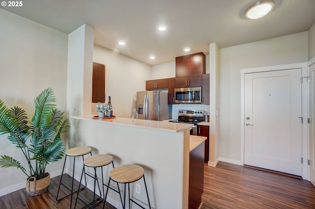 16417 NW Chadwick Way Unit 302, Portland, OR 97229 - kitchen featuring stainless steel appliances, dark wood-style flooring, a kitchen bar, light countertops, and recessed lighting