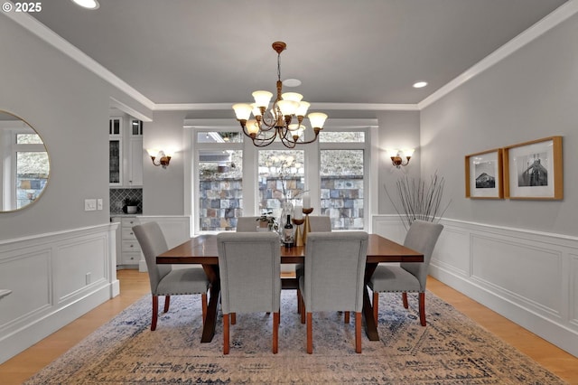 dining space featuring a wainscoted wall, light wood-type flooring, a chandelier, and ornamental molding