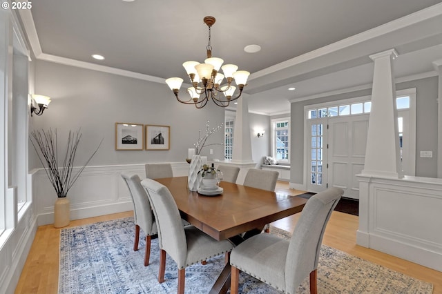 dining area featuring a wainscoted wall, ornate columns, light wood-style flooring, crown molding, and a decorative wall