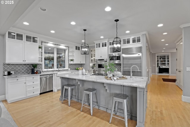 kitchen featuring built in appliances, a large island with sink, and white cabinets