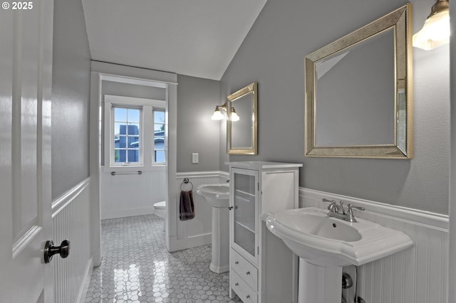 bathroom featuring tile patterned flooring, wainscoting, toilet, and vaulted ceiling