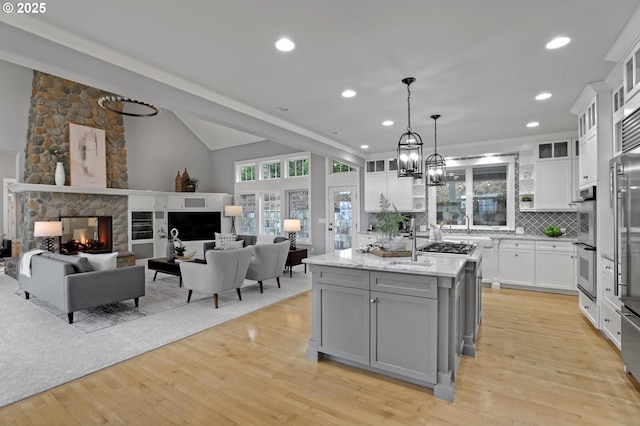 kitchen with light wood-style flooring, gray cabinets, a stone fireplace, white cabinetry, and open floor plan