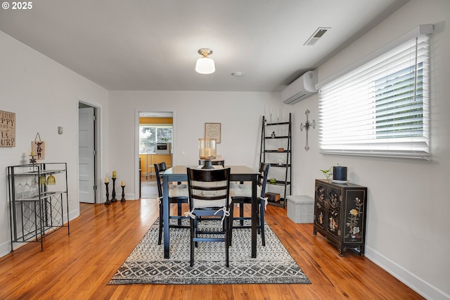 dining room with baseboards, an AC wall unit, wood finished floors, and visible vents